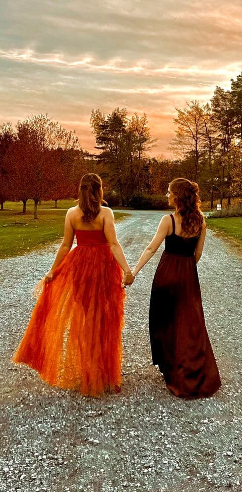 The original phone photograph of two women in gowns holding hands on a gravel road at sunset.